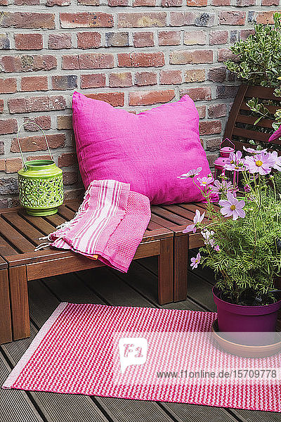Balcony with bench pink cushion blanket lantern mat and various potted plants