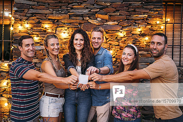 Gruppenporträt glücklicher Freunde im Freien an einem Steinhaus mit einer leeren Karte