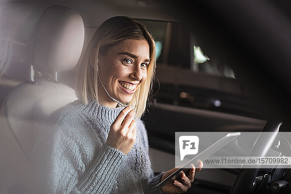 Glückliche junge Frau mit Tablette und Kopfhörern in einem Auto