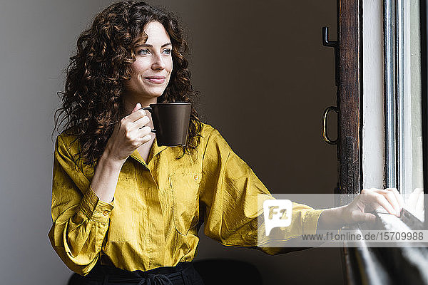 Frau schaut mit Kaffeetasse aus dem Fenster