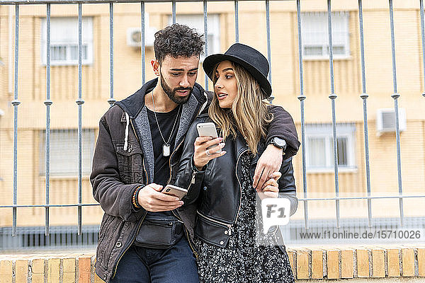 Junges Ehepaar in der Stadt bei der Benutzung ihres Mobiltelefons