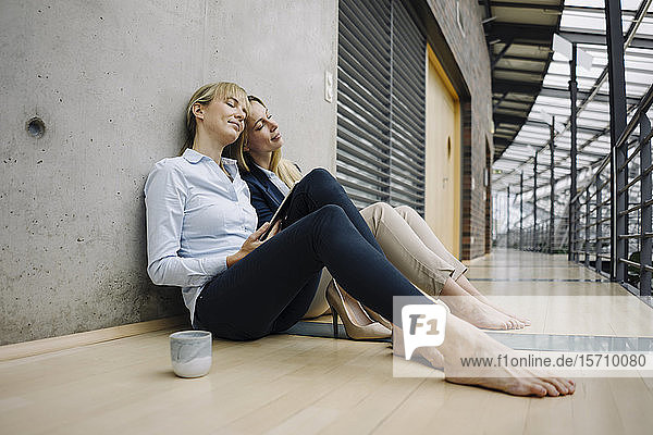 Zwei junge Geschäftsfrauen machen eine Pause im Büro und sitzen auf dem Boden