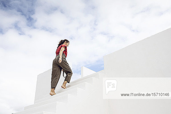 Barefooted businesswman climbing white stairs under cloudy sky