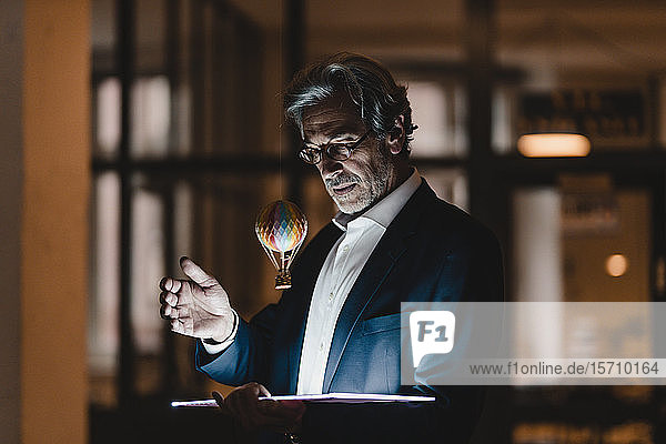 Senior businessman with tablet and floating hot-air balloon in office