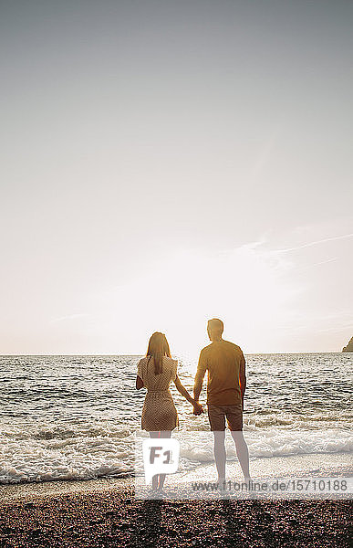 Rückansicht eines jungen Paares am Strand bei Sonnenuntergang