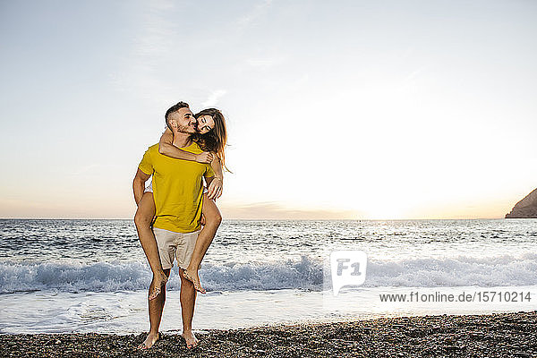 Young couple at the beach at sunset  man carrying laughing woman