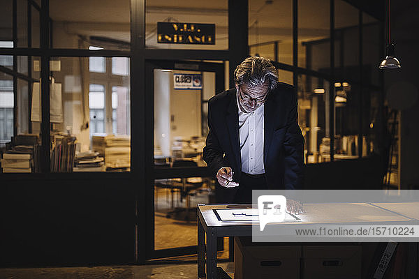 Senior businessman looking at shining tablet in office