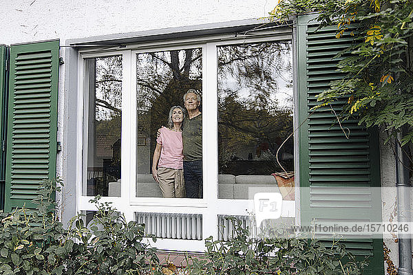 Älteres Ehepaar hinter der Fensterscheibe seines Hauses mit Blick nach draußen
