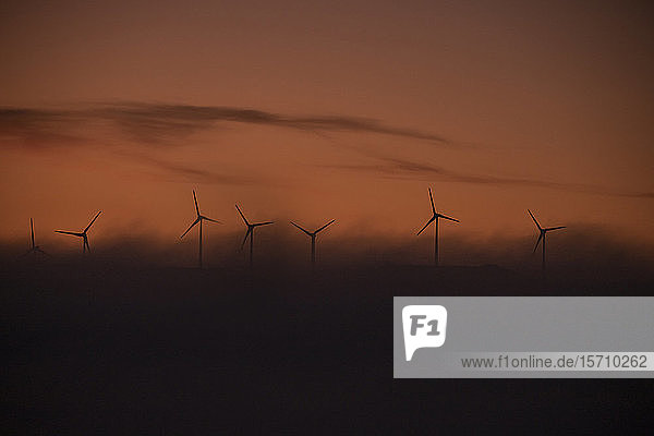 Spanien  Provinz Cádiz  Tarifa  Silhouetten von Windturbinen  die bei nebliger Morgendämmerung vor launischem Himmel stehen