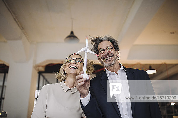 Happy businessman and businesswoman holding wind turbine model in office