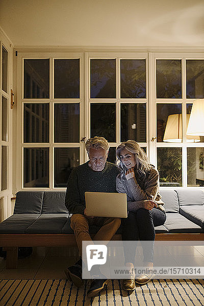 Senior couple using laptop on couch at home at night