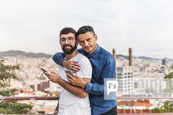 Porträt eines glücklichen schwulen Paares mit Smartphones  Barcelona  Spanien