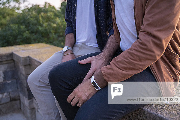 Close-up of affectionate gay couple sitting on a wall