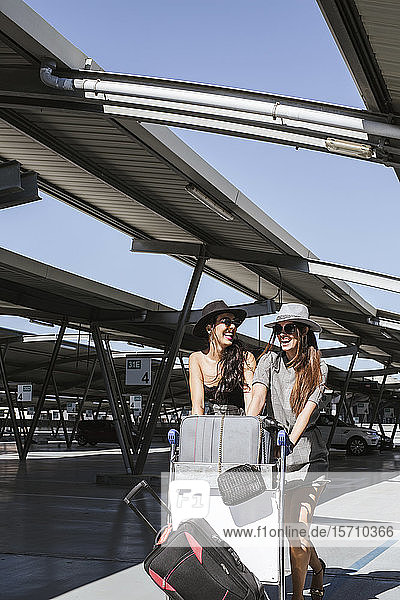 Zwei fröhliche  modische junge Frauen mit Gepäck auf dem Flughafen-Parkdeck