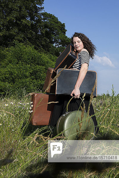 Porträt einer jungen Frau auf einer Wiese mit vielen Koffern