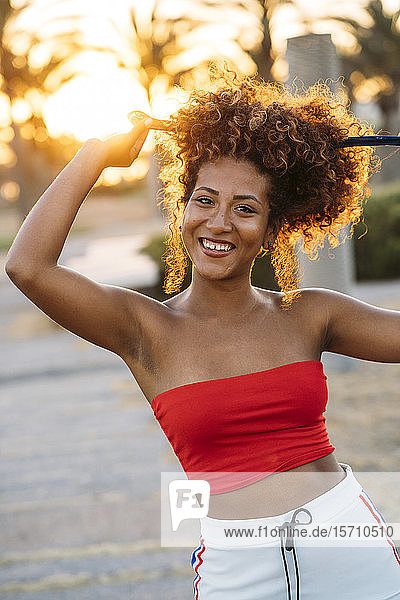Porträt einer glücklichen Frau  die sich bei Sonnenuntergang die Haare bindet