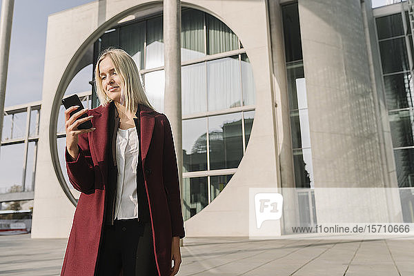 Blond businesswoman using smartphone in the background modern building