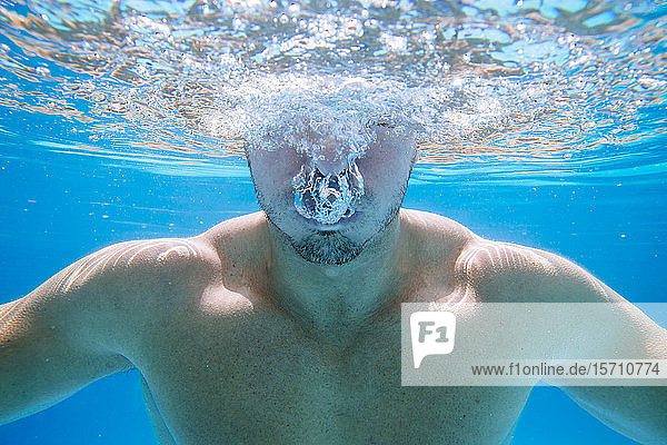 Unterwasseraufnahme eines Mannes im Schwimmbad  der Blasen aus dem Mund bläst