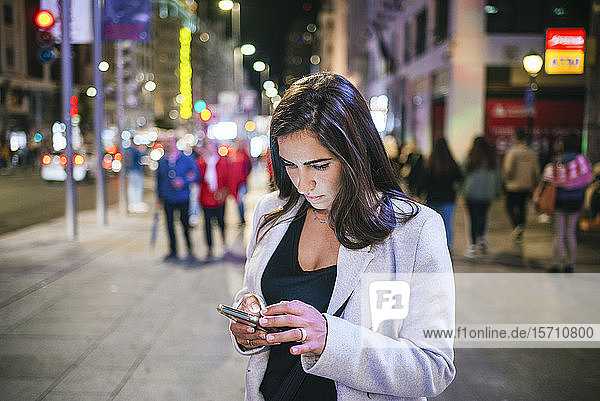 Frau benutzt ihr Smartphone nachts auf der Straße
