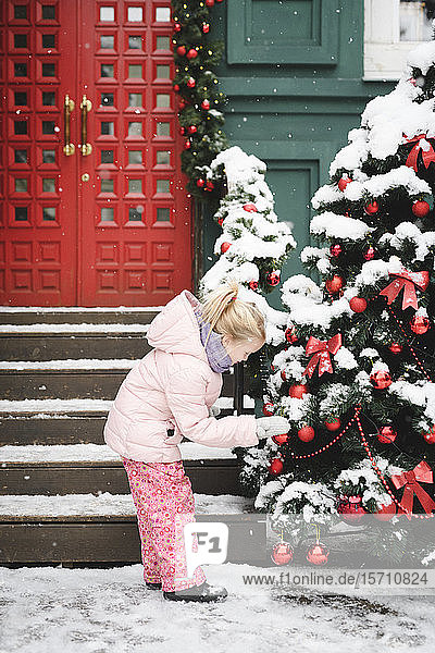 Kleines Mädchen beobachtet Weihnachtskugeln am Weihnachtsbaum im Freien