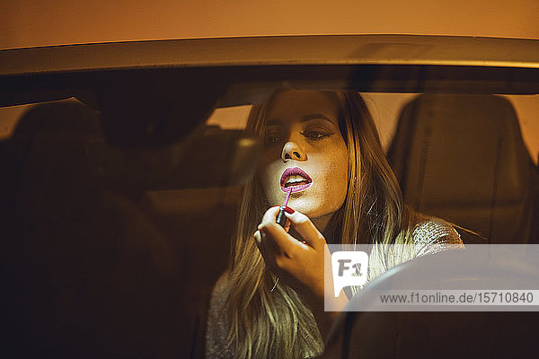Porträt einer blonden Frau im Auto beim Auftragen von Lippenstift