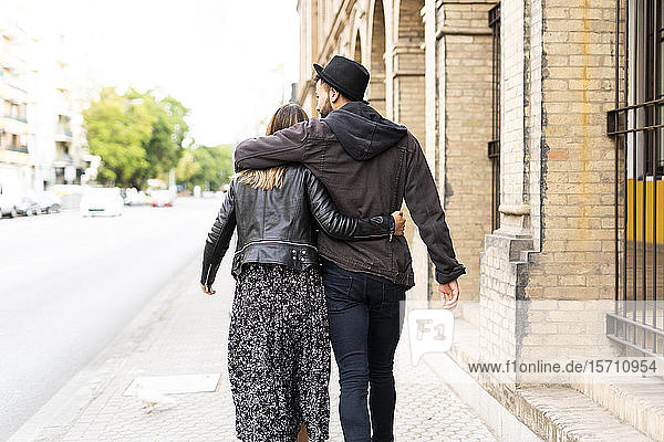 Back view of young couple in love walking arm in arm in the city
