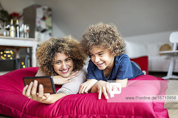 Mutter und Sohn sehen sich ein Video auf einem Smartphone an und liegen auf einem großen Kissen