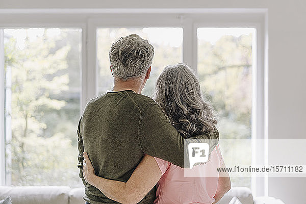Rückansicht eines älteren Ehepaares das zu Hause aus dem Fenster schaut