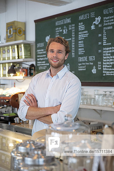 Junger Geschäftsmann in einem Cafe  mit verschränkten Armen hinter der Theke