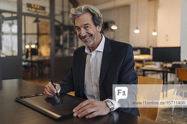 Portrait eines lächelnden älteren Geschäftsmannes mit Grafiktablett am Schreibtisch im Büro