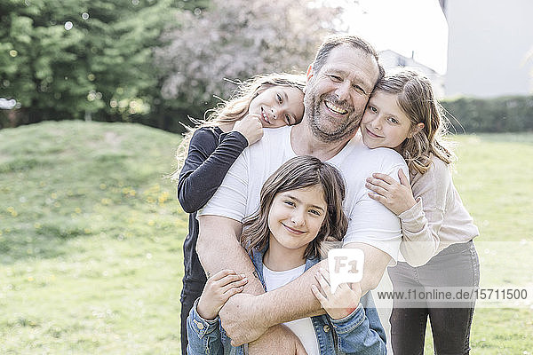 Porträt eines glücklichen Vaters mit drei Drillings-Töchtern auf einer Wiese