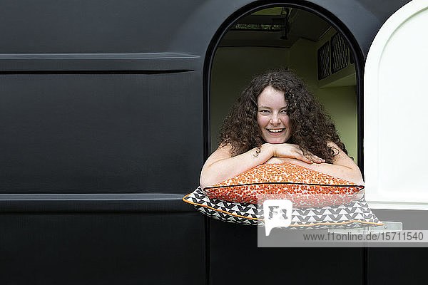 Porträt einer lachenden  auf Kissen gelehnten jungen Frau  die aus dem Wohnwagen schaut
