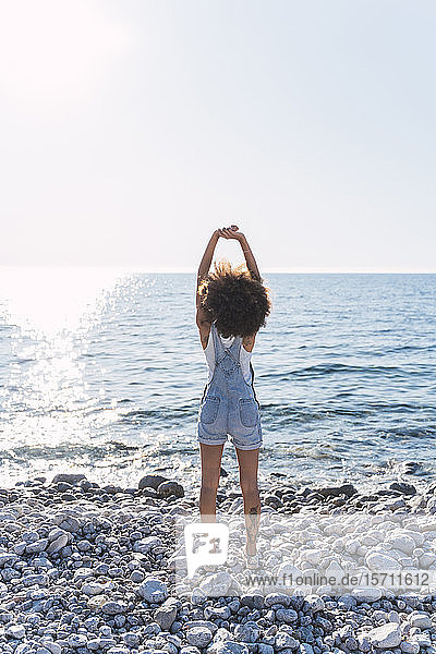 Rückansicht einer jungen Frau am Strand  die ihre Arme ausstreckt