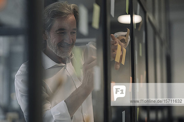 Leitender Geschäftsmann bringt Klebezettel an Glasscheibe im Büro an