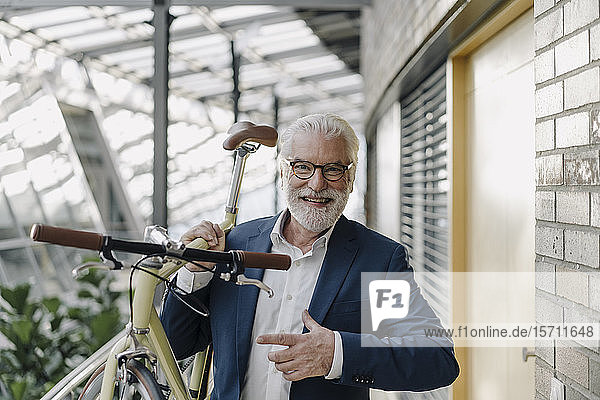 Porträt eines glücklichen älteren Geschäftsmannes mit einem Fahrrad in einem modernen Bürogebäude