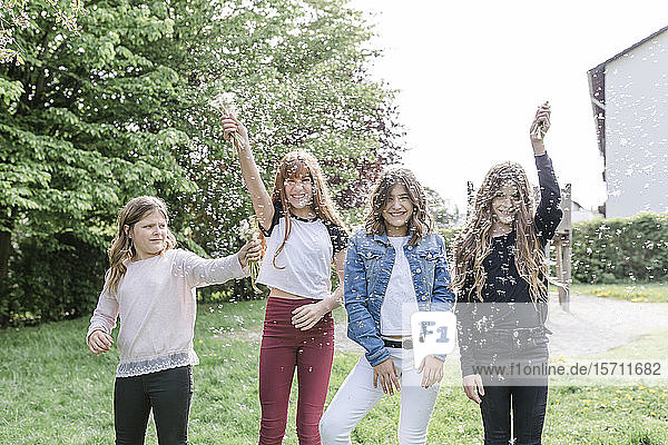 Four happy girls playing with dandelion seeds