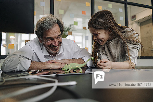 Happy senior buisinessman and girl playing with chameleon figurine in office
