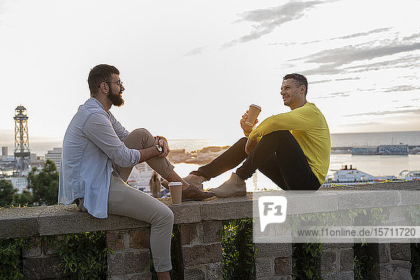 Two men sitting on a wall on lookout above the city with view to the port  Barcelona  Spain