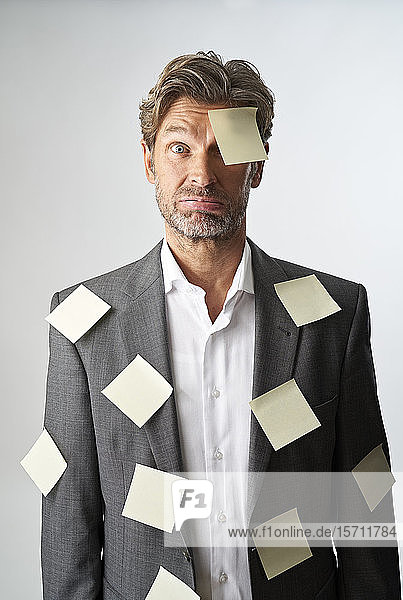 Porträt eines hilflosen Geschäftsmannes mit auf die Stirn geklebten Zetteln und Anzugmantel