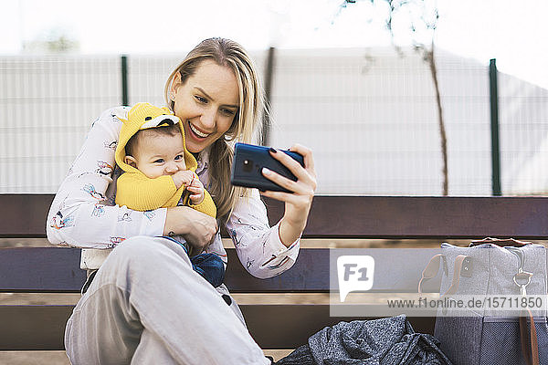 Glückliche Mutter ruht sich mit dem kleinen Jungen auf einer Parkbank aus und nimmt ein Selfie