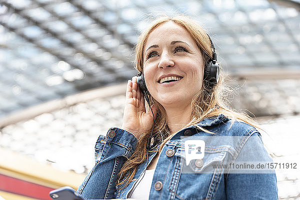 Glückliche Frau  die am Bahnhof mit Kopfhörern Musik hört  Berlin  Deutschland