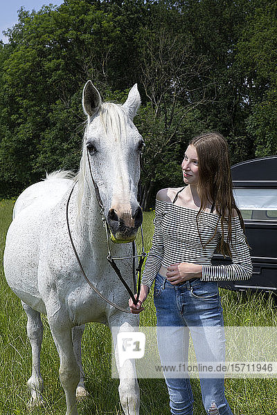 Glückliche Teenagerin mit Pferd auf der Wiese stehend