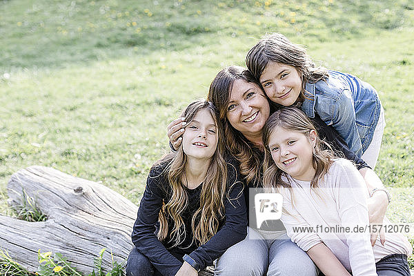 Porträt einer lächelnden Mutter mit drei Drillings-Töchtern auf einer Wiese