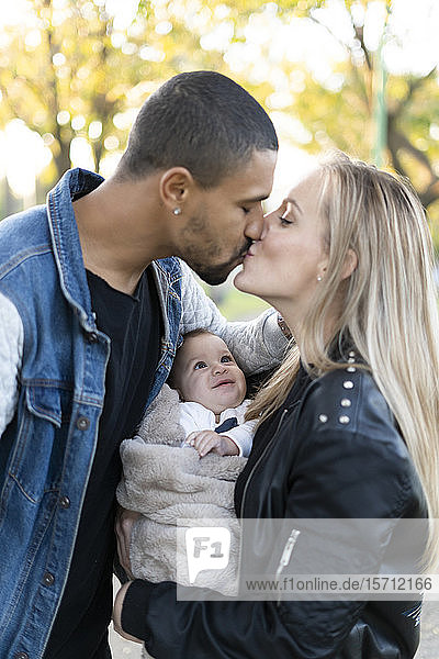 Glückliche Eltern küssen sich im Park  mit einem kleinen Sohn zwischen ihnen