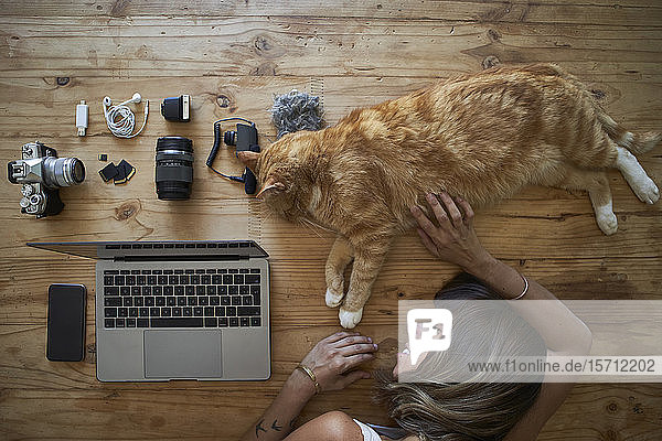 Exhausted woman sleeping on table with ginger cat laptop and photografic equipment