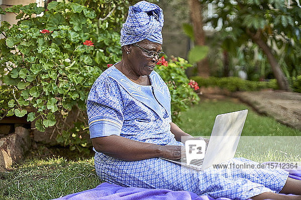 Ältere Frau sitzt mit Laptop auf dem Rasen