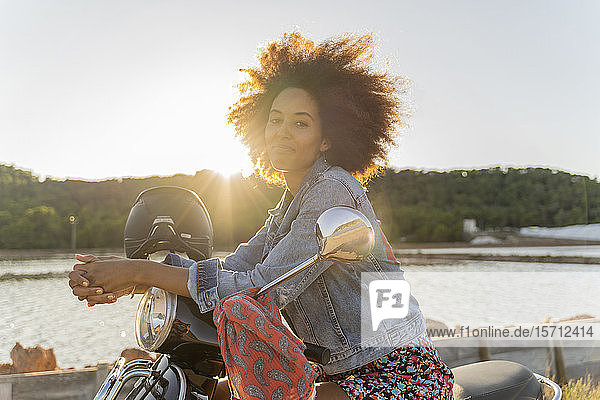Junge Frau sitzt bei Sonnenuntergang auf einem Motorroller  Ibiza