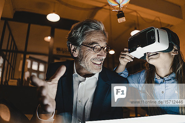 Happy senior buisinessman and girl wearing VR glasses with hot-air balloon in office