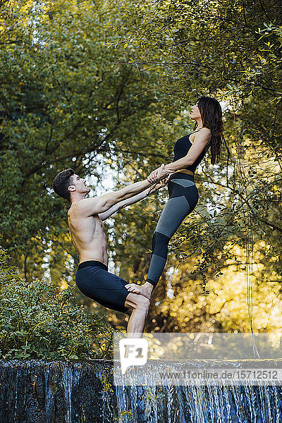 Ein Paar  das gemeinsam Akro-Yoga an einem Wasserfall praktiziert
