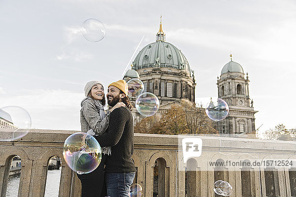 Glückliches junges Paar umarmt beim Betrachten von Seifenblasen in der Stadt  Berlin  Deutschland